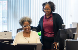 two women smile while facing a computer